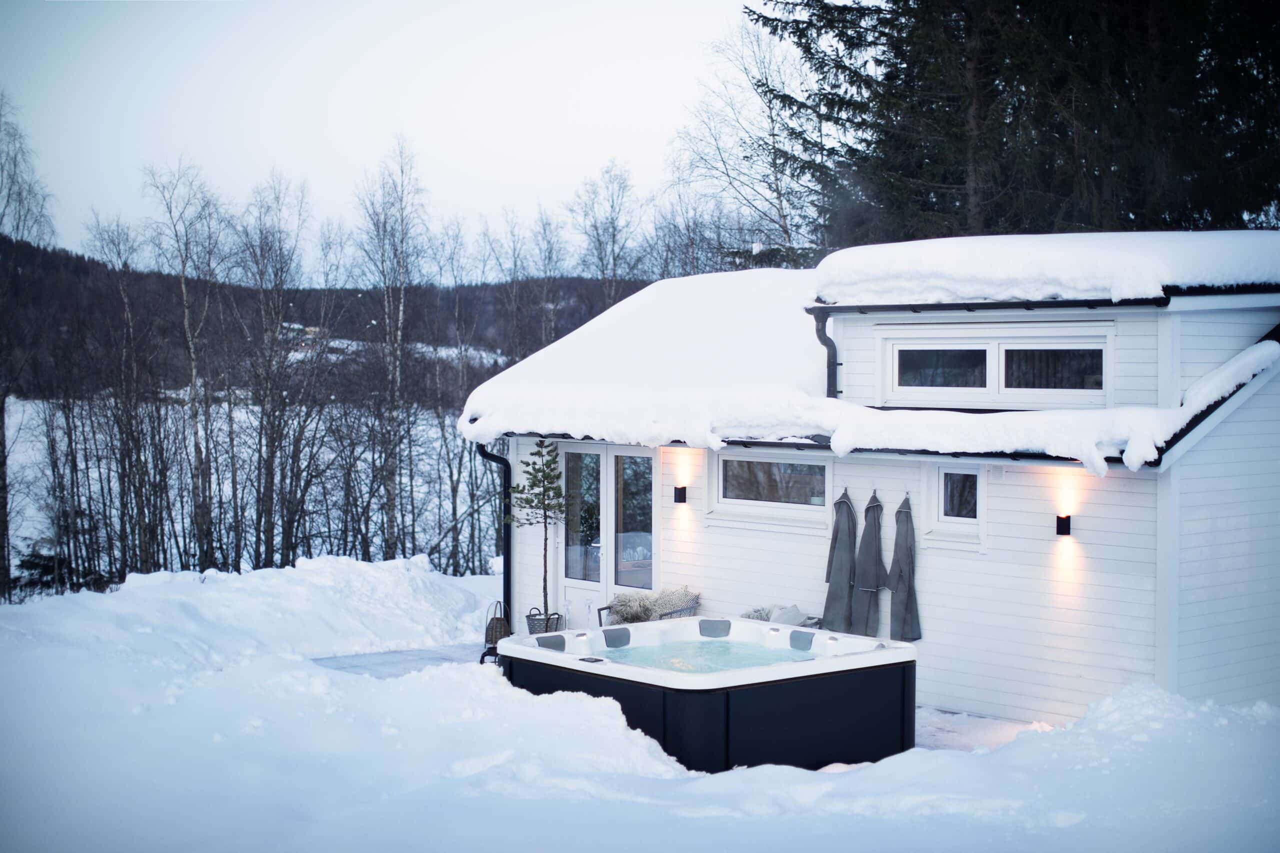 Vitt attefallshus i vintermiljö med en jacuzzi